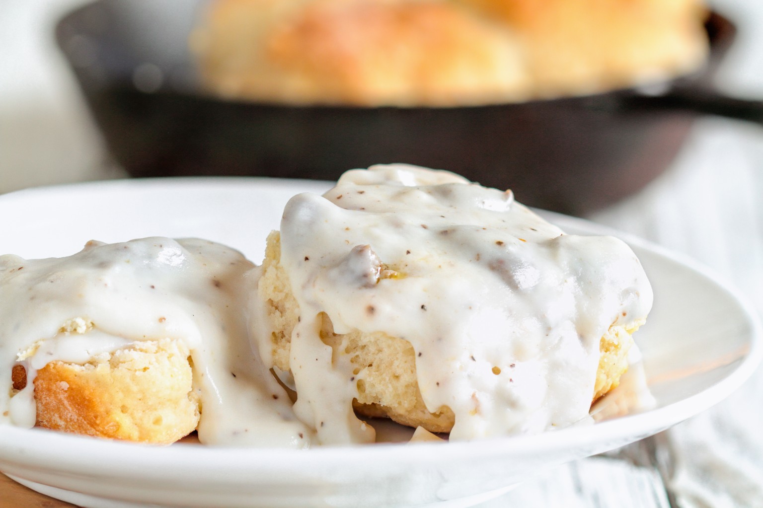 Biscuits topped with creamy pepper-speckled gravy on a white plate.