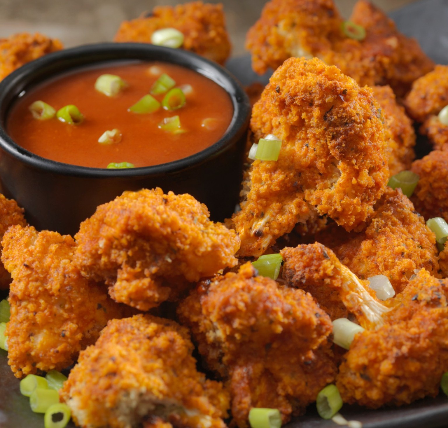 Golden fried cauliflower florets with sliced green onions and a bowl of dipping sauce.