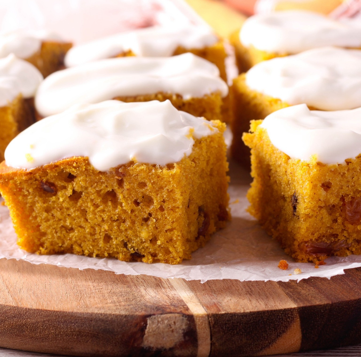 Squares of pumpkin cake topped with cream cheese frosting on a wooden board.