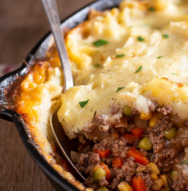 Potato-topped pie with a browned filling, peas, carrots, and corn in a skillet.